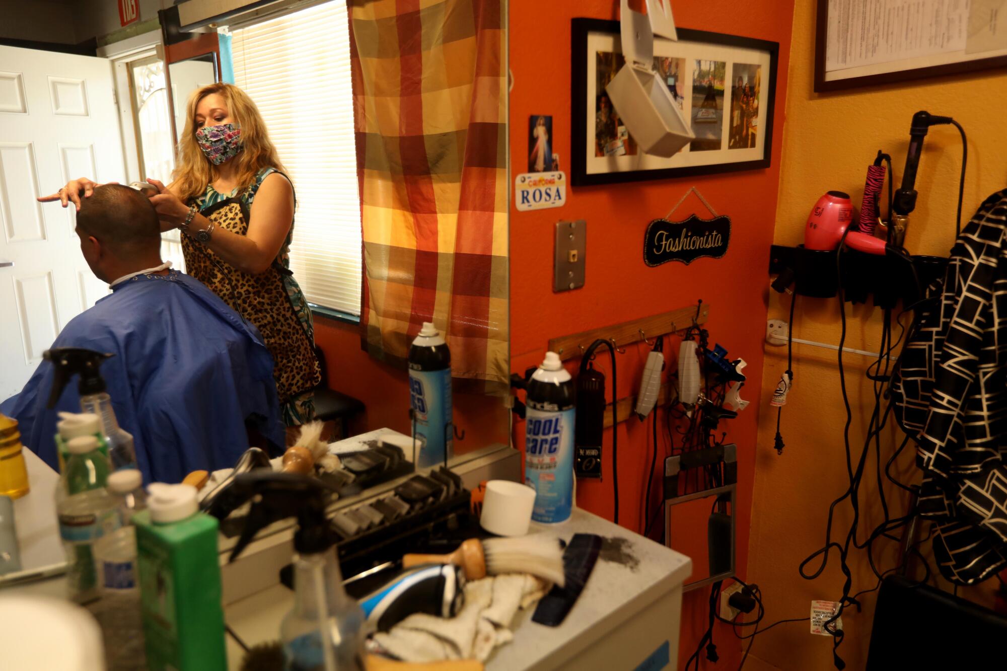 Rosa Pedraza, wearing a protective mask, cuts Robert Nunez' hair at Rosa's Hair Salon in Atwater.