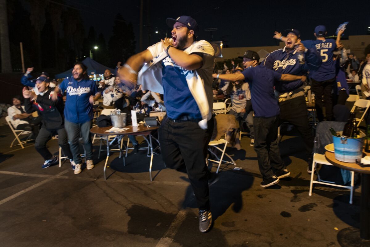 Dodgers fans jump and pump their fists at tables set up in an outdoor parking lot