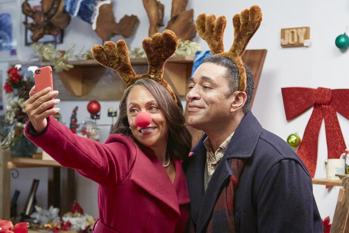 Liza Huget and Harry Lennix take a photo together in a scene from "A Christmas Together With You" on Hallmark