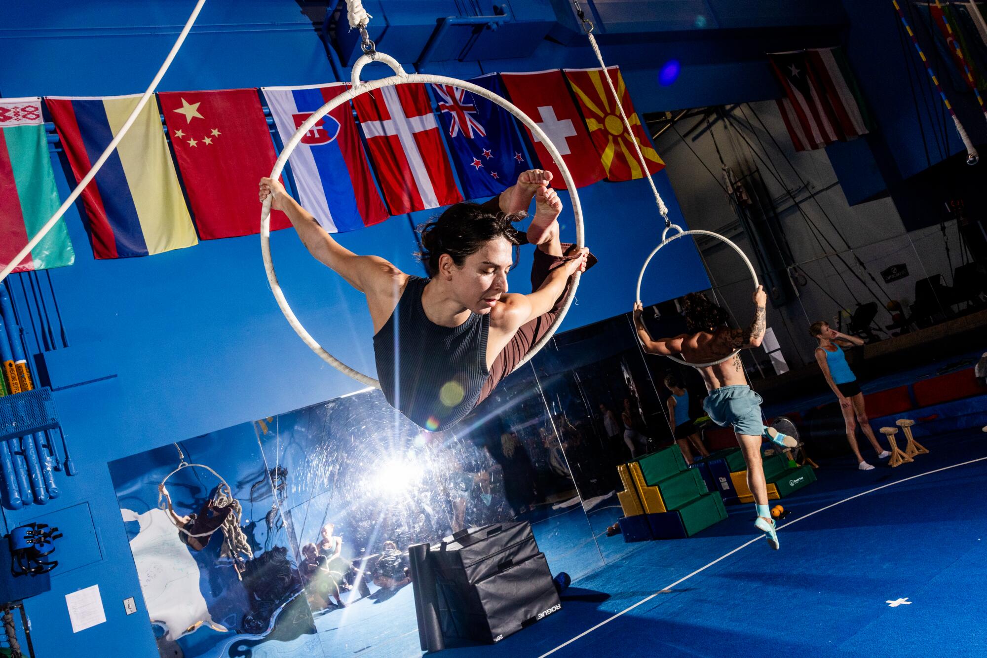Cirque du Soleil cast members train at the gym, which has flags on the walls. 