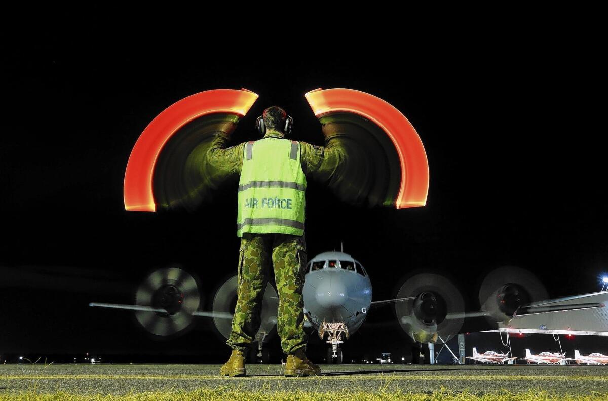 A ground crew member directs an Australian air force plane upon its return to the Pearce air base near Perth after it took part in a search for the Malaysia Airlines jetliner.