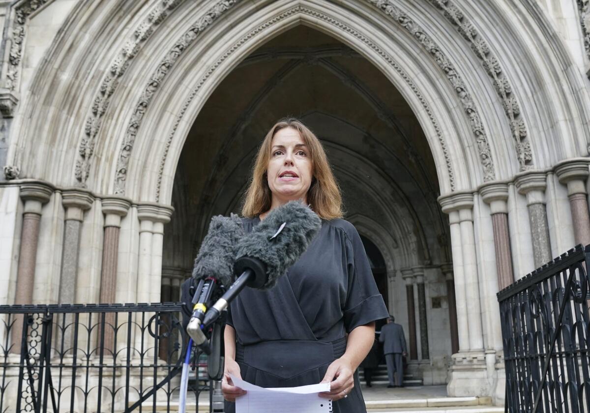 A woman speaks into microphones outside Royal Courts of Justice, in London.