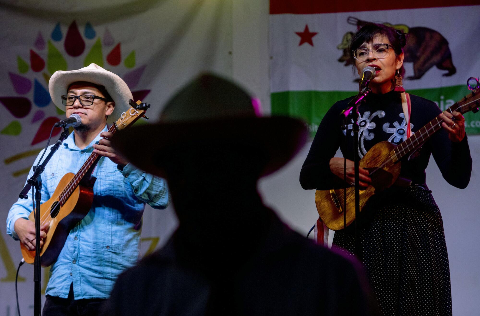 Cesar Castro and Xochi Flores of Jarochelo play onstage while dancers perform.