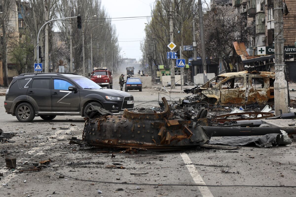 A blackened piece of a tank sits in a city street.
