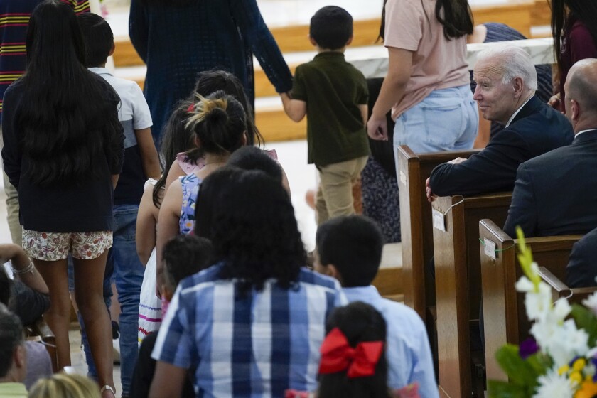 Children walk to the front of a church sanctuary as President Biden watches from a pew.