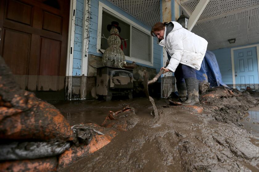 SANTIAGO CANYON, CALIF. - MAR. 10, 2021. Santiago Canyon resident Linda Learned clears mud away from her front door after a slide caused by heavy rain sent torrents of water and debris downhill on Wednesday morning, Mar. 10, 2021. Surrounding mountains were badly burned during wildfires last year. (Luis Sinco/Los Angeles Times)