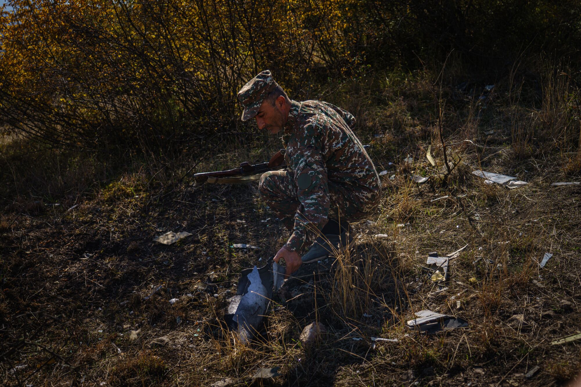 A man in fatigues examines a drone remnant on a hillside in Nagorno-Karabakh.