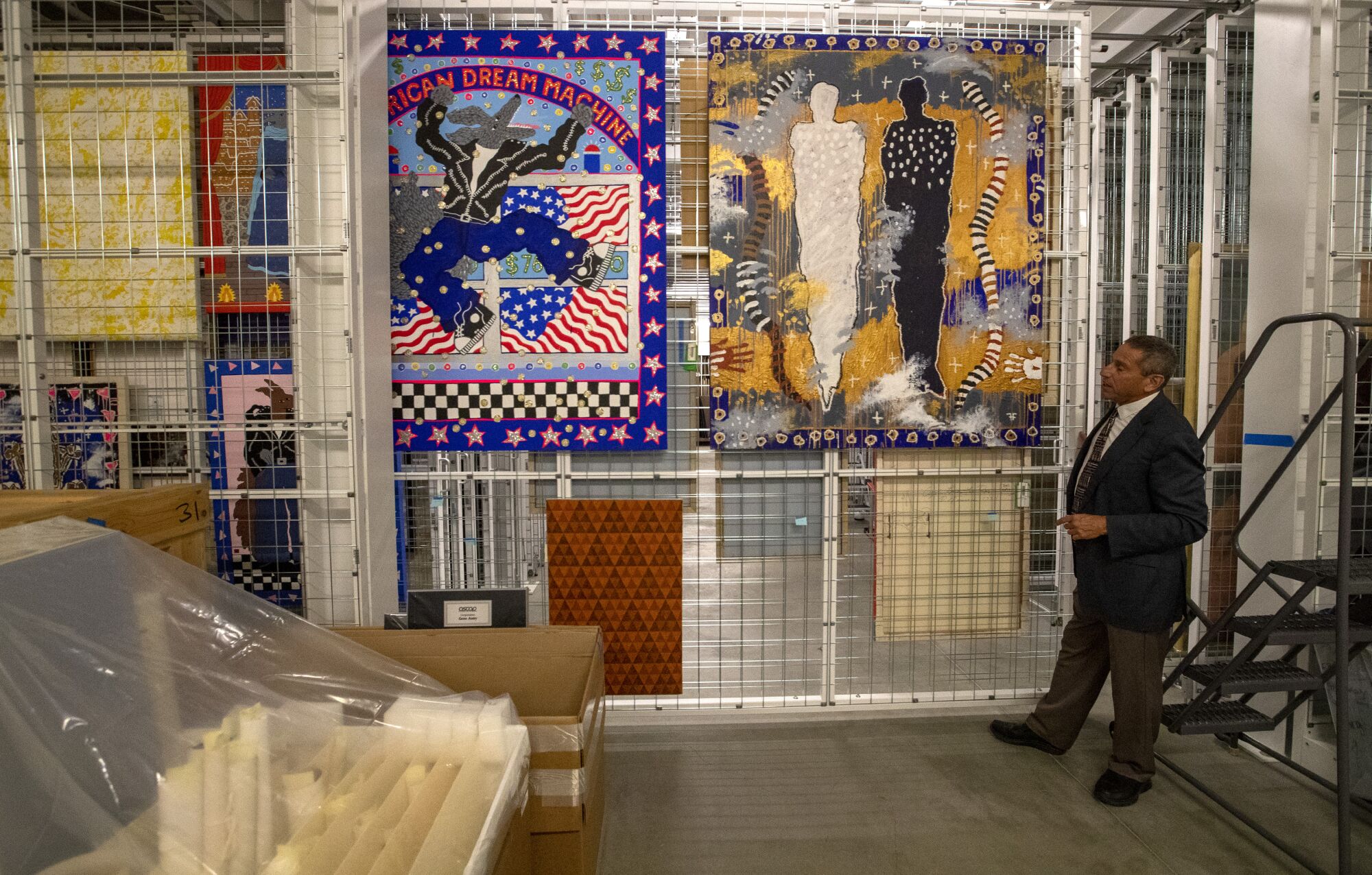 A man stands behind paintings hanging in a storage facility