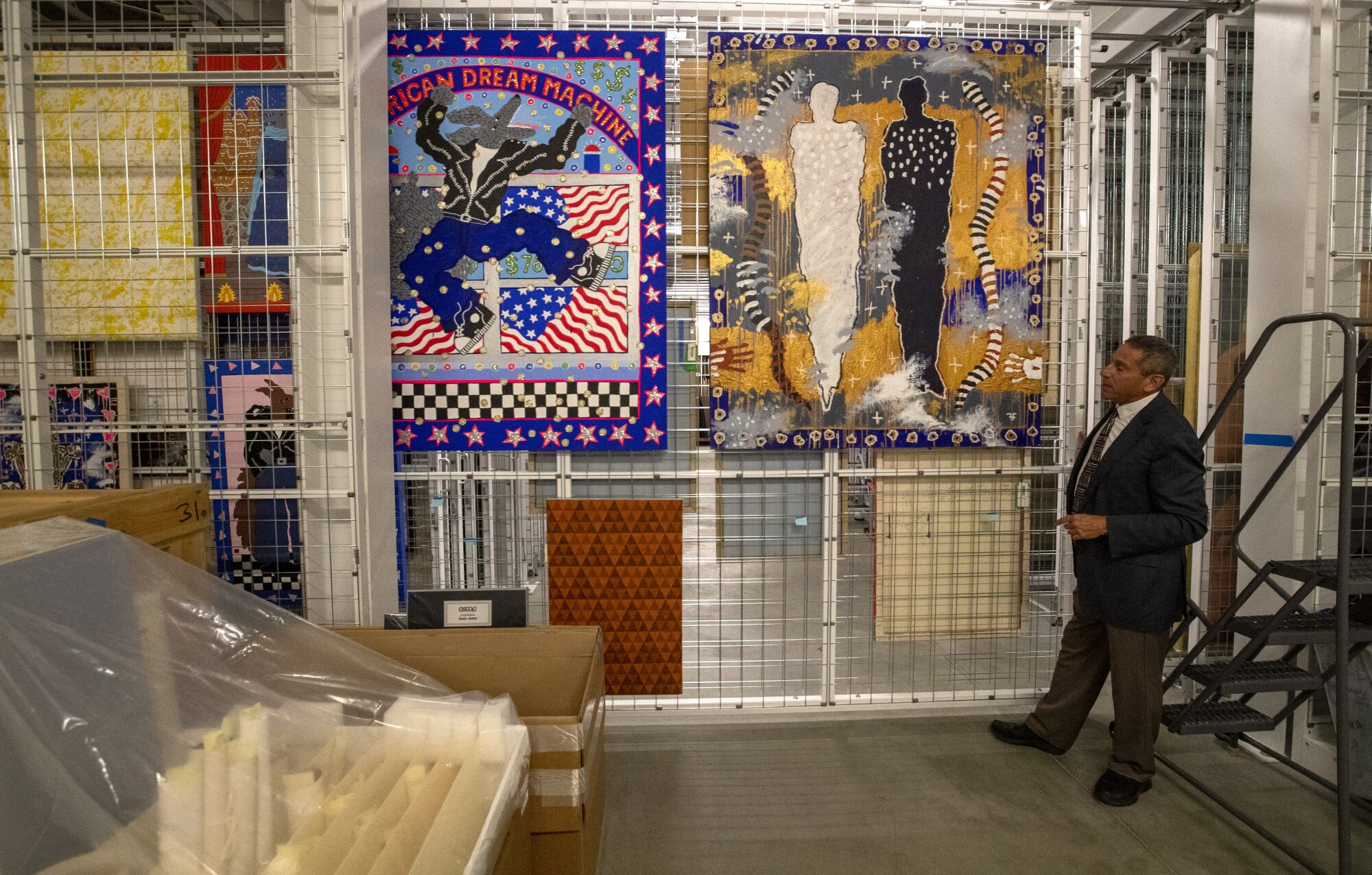 A man stands behind paintings hanging in a storage facility 