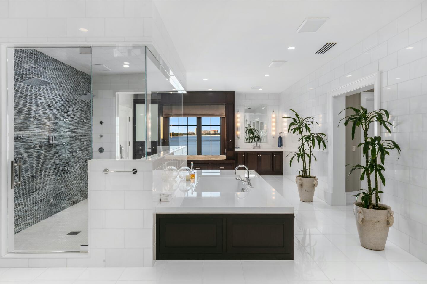 A large, rectangular, modern bathtub is next to a white shower with small gray tiles.
