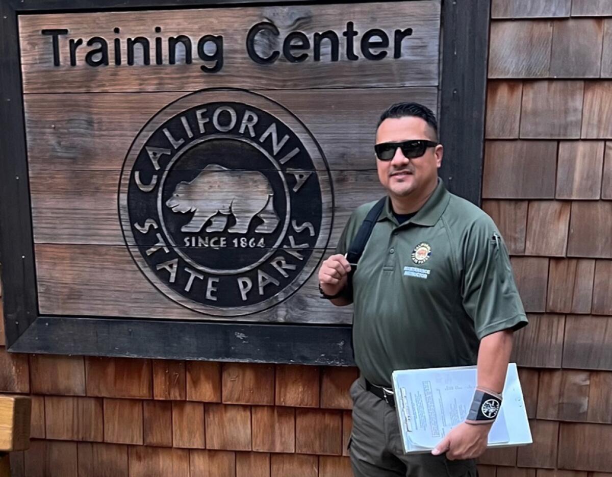 A man wearing sunglasses stands in front of a California State Parks training center sign