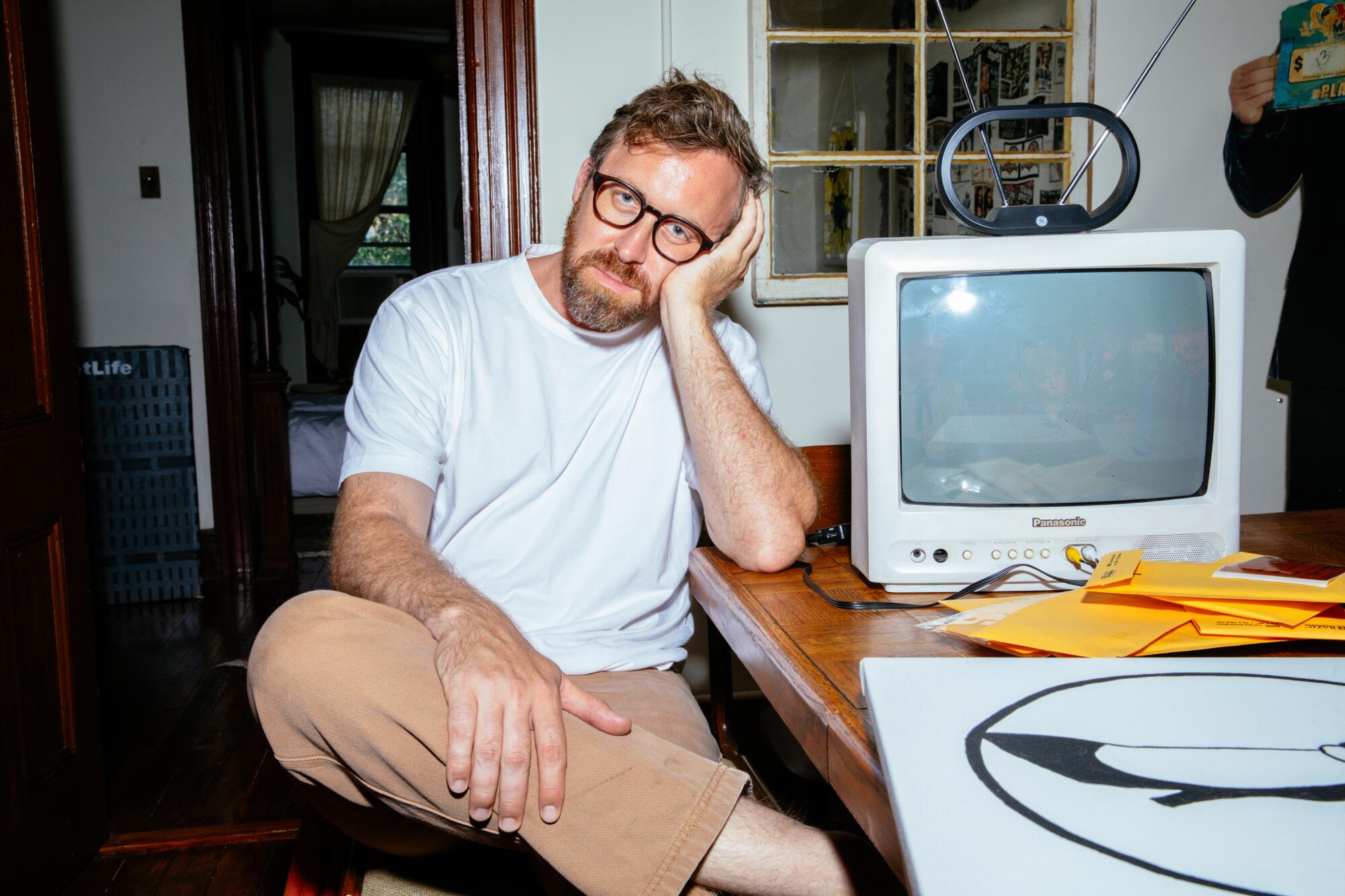 John Wilson sitting next to an old TV inside a house.