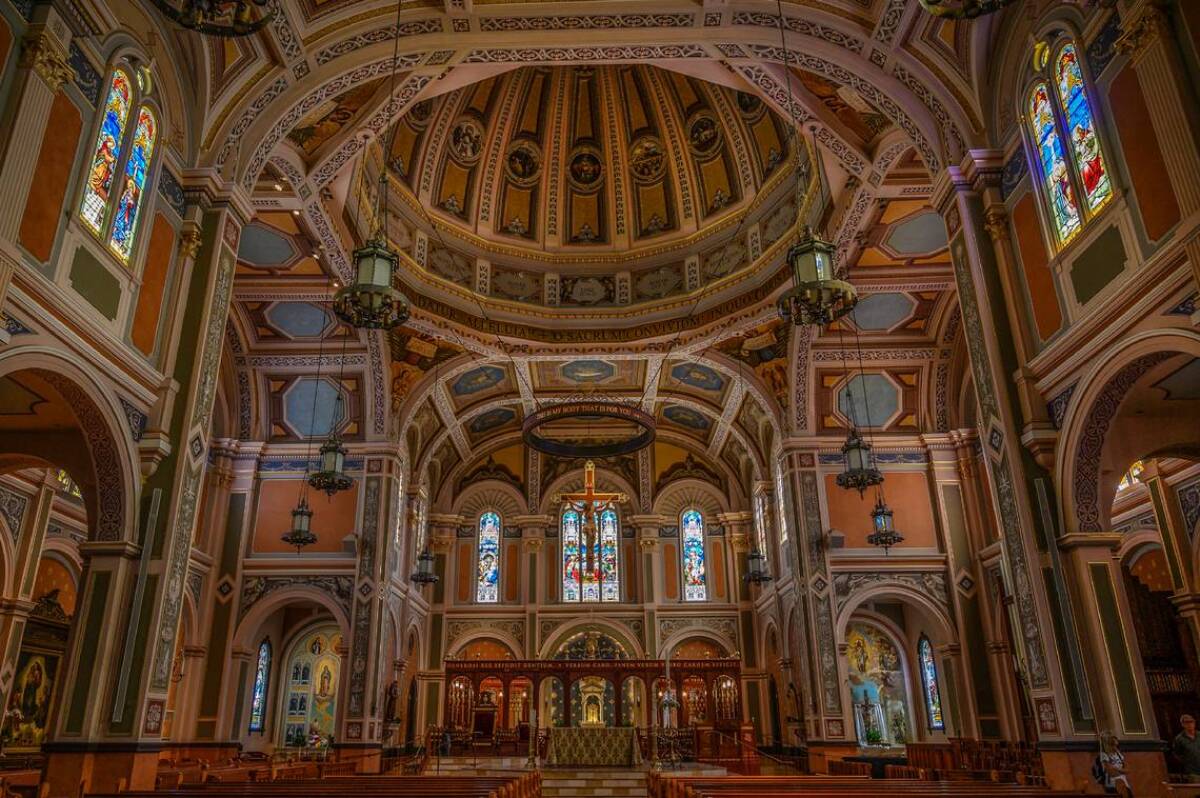 The interior of a soaring Catholic church with a dome and stained glass windows.