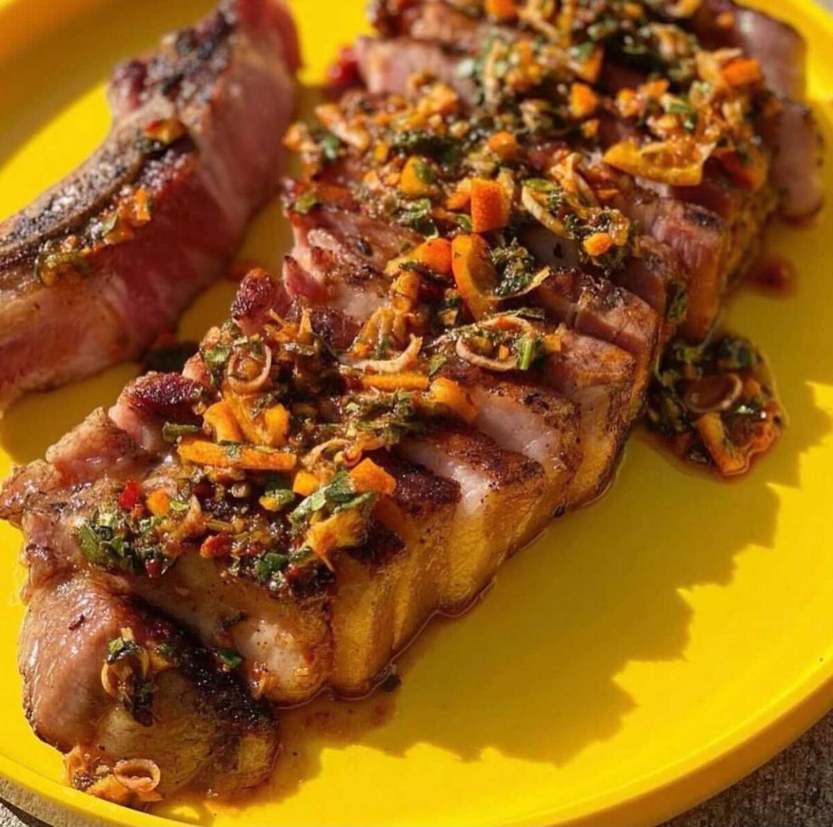 A pork chop on a yellow plate covered with a sauce with diced vegetables.