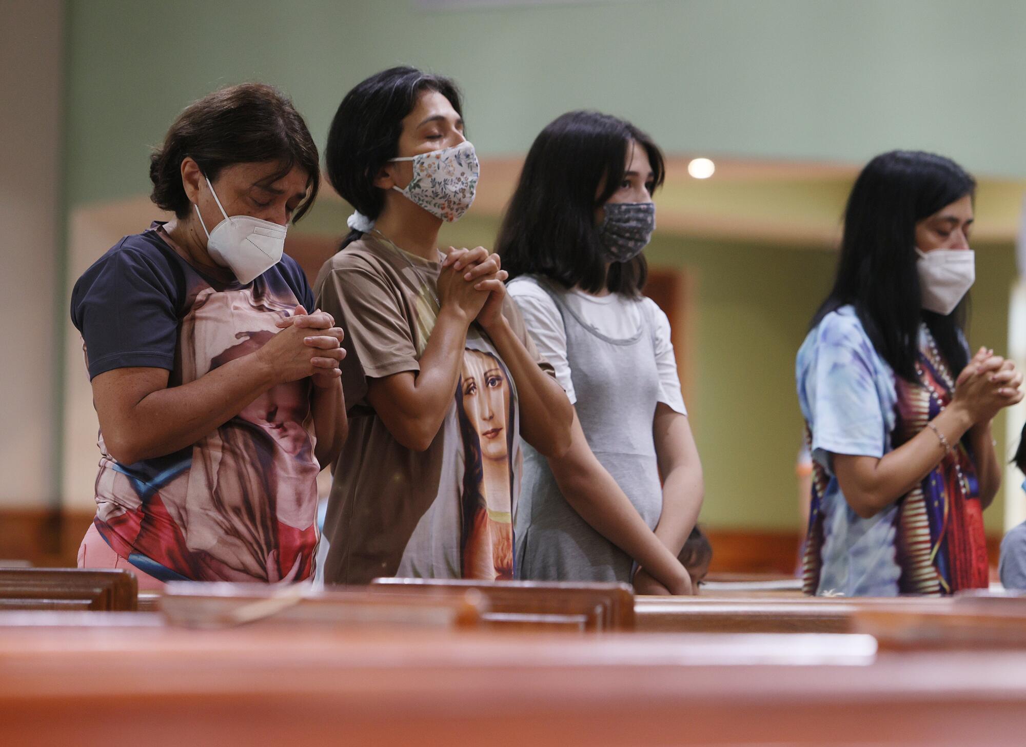 Women and girls in masks stand and pray inside a church.