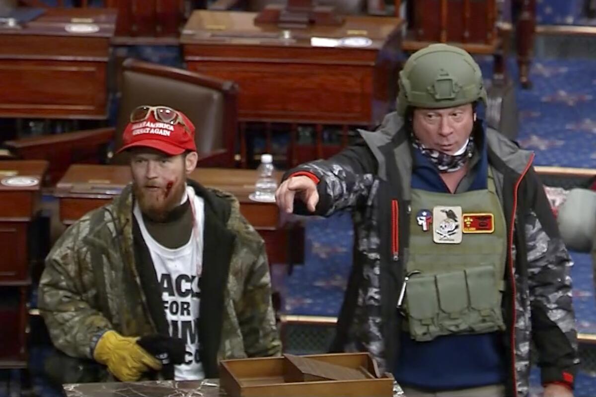 A man in military gear and a man in a red baseball cap in the Senate chamber
