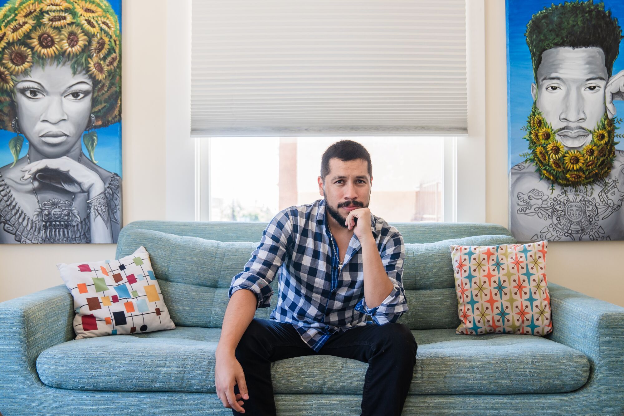 Muralist Hervey Garcia sits near his paintings, "Sunflower Goddess" and "Sunflower God," in Hillcrest.