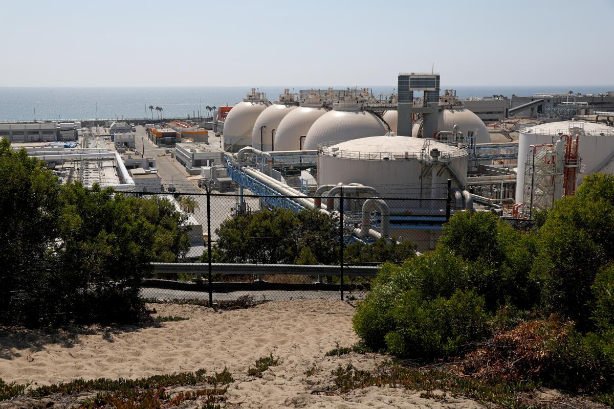 Large tanks from an industrial facility are pictured beside an ocean.