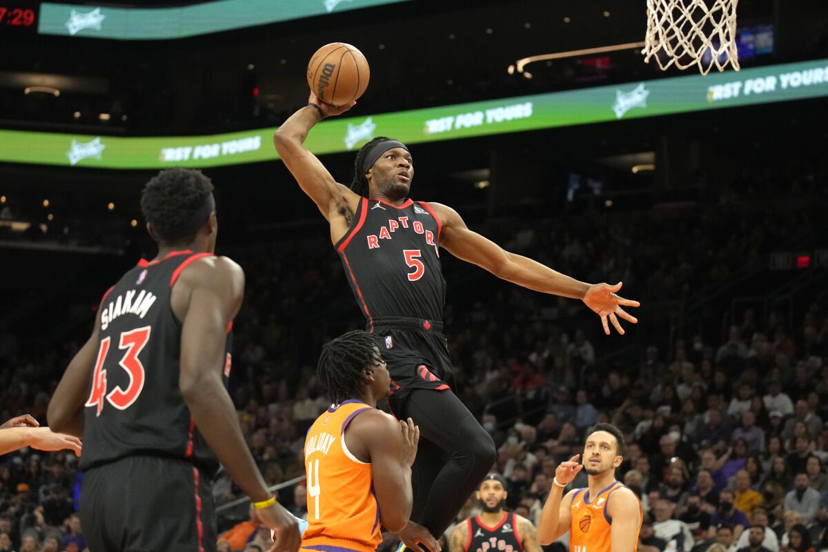 Toronto Raptors forward Precious Achiuwa (5) dunks over Phoenix Suns guard Aaron Holiday (4) and guard Landry Shamet, right, during the first half of an NBA basketball game, Friday, March 11, 2022, in Phoenix. (AP Photo/Rick Scuteri)
