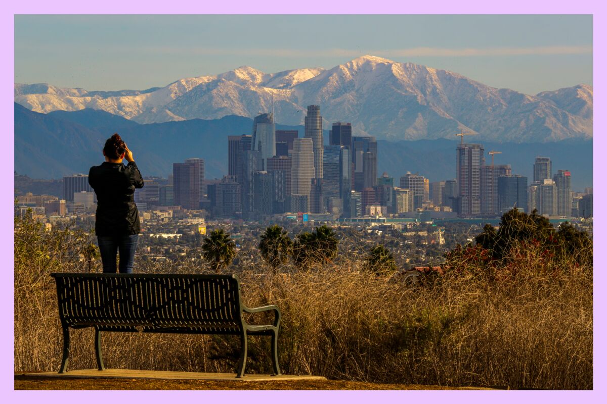 A person stands on a bench to photograph the downtown Los Angeles skyline from Kenneth Hahn State Recreation Area.