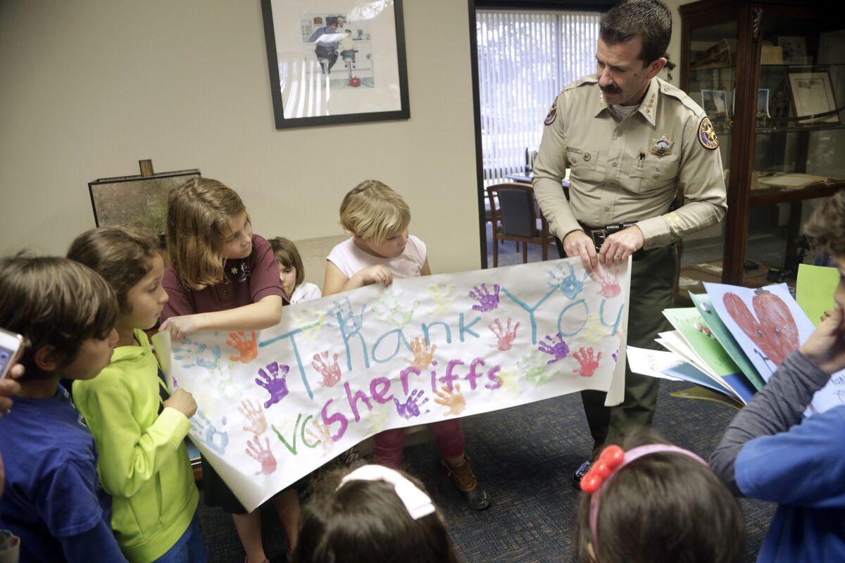 Ventura County Sheriff Bill Ayub is greeted by a group of children from KidStream Children's Museum in Ventura County with thank-you cards and a poster.