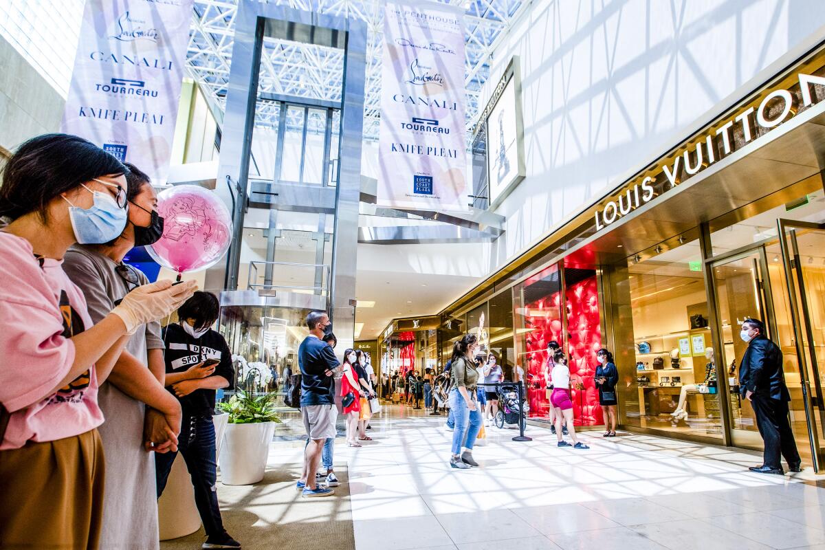 Shoppers wearing masks in an indoor shopping mall outside a Louis Vuitton store.