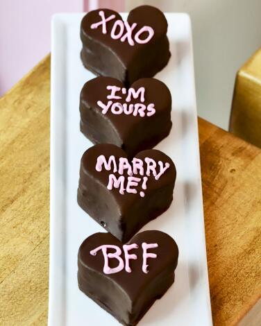 Four heart-shaped chocolate mini cakes with sweet messages such as "BFF" on them