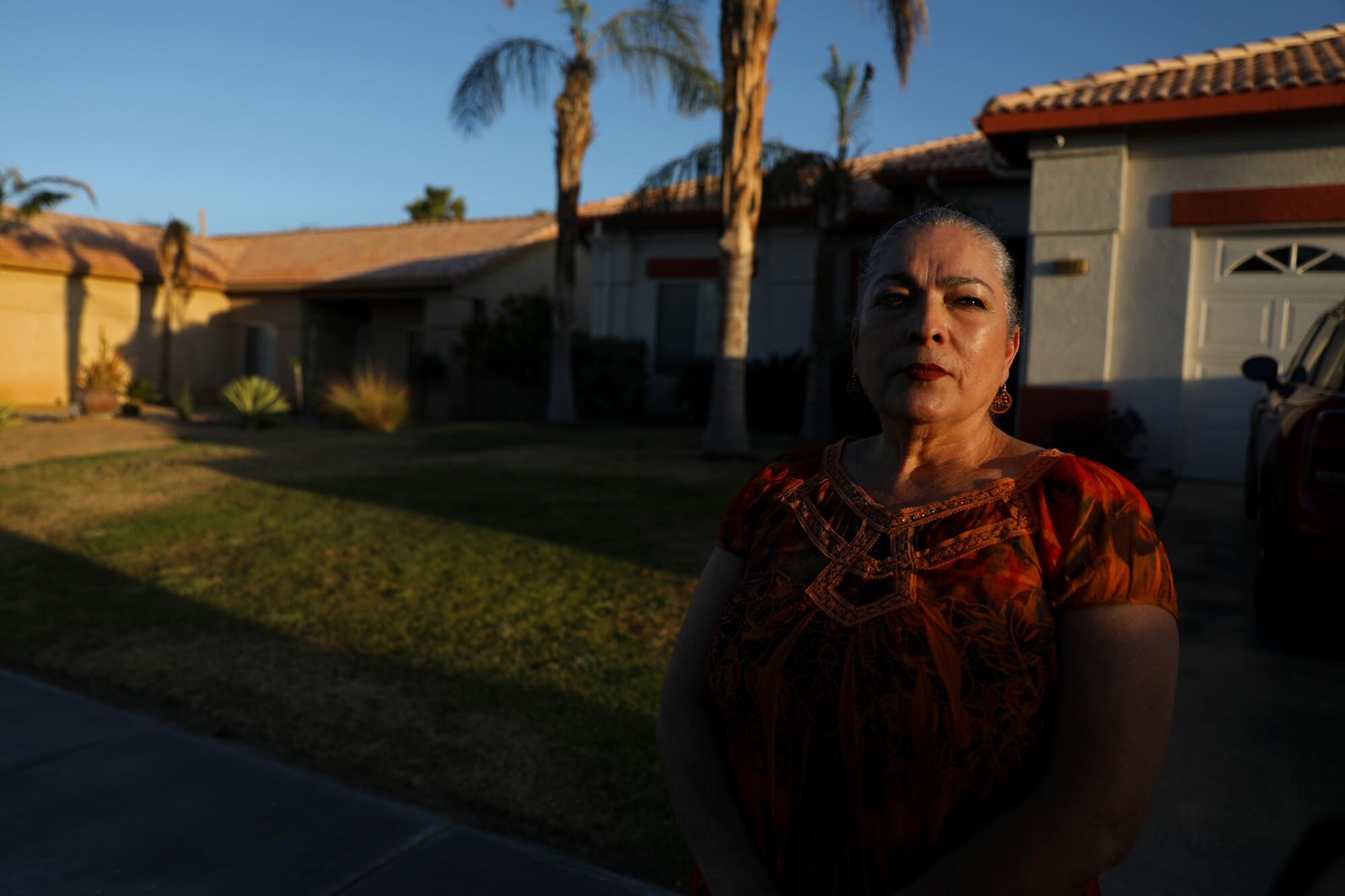 A woman stands in front of a home with palm trees 