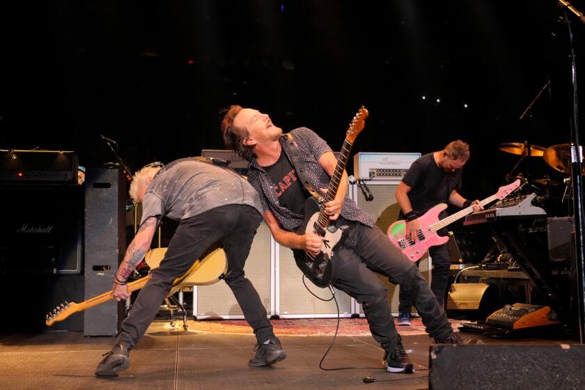 Mike McCready and Eddie Vedder and members of Pearl Jam are leaning against each other while strumming guitars on stage