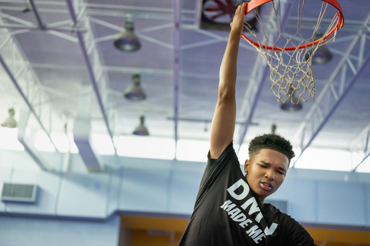 A teenager in a black T-shirt dunks a basketball