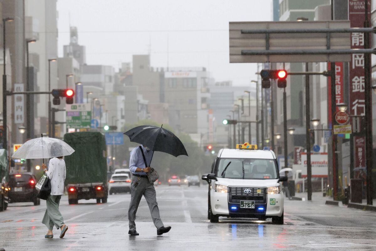 People walk in the rain in front of a station, Saturday, Aug. 13, 2022, in Shizuoka, west of Tokyo. Tropical Storm Meari is unleashing heavy rains on southwestern Japan as it heads northward toward the Tokyo capital, according to Japanese weather officials. (Kyodo News via AP)