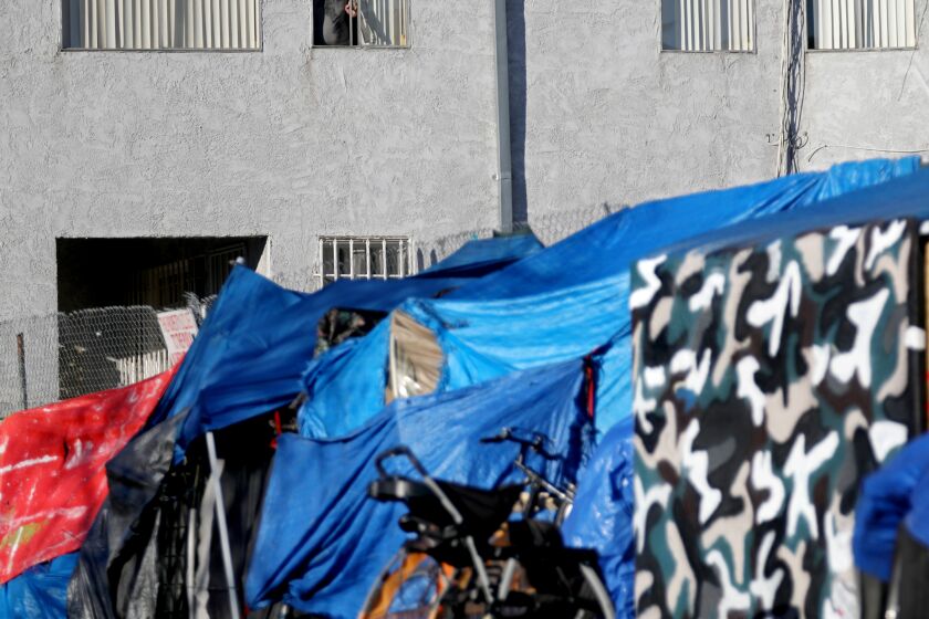 LOS ANGELES, CA - FEBRUARY 18: A man looks out his window of his apartment as a homeless encampment blocks the sidewalk along the 1800 block of N Berendo St and Hollywood Blvd in the Los Feliz neighborhood on Thursday, Feb. 18, 2021 in Los Angeles, CA. Residents of N Berendo St. have been begging city officials for help with homeless encampments that block the sidewalk. The Berendo tent population is more aggressive than the more traditional homeless population on Hollywood Blvd threatening retaliation against residents. (Gary Coronado / Los Angeles Times)