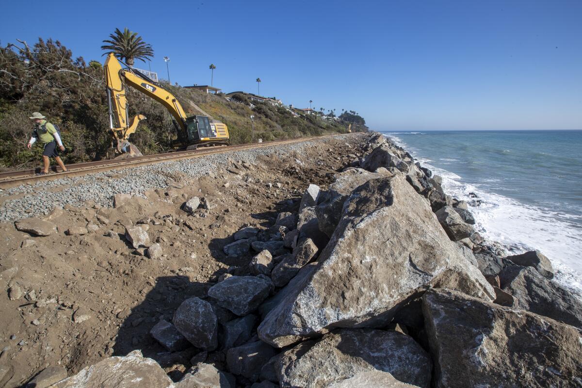A person and heavy machinery next to big rocks by a coast.