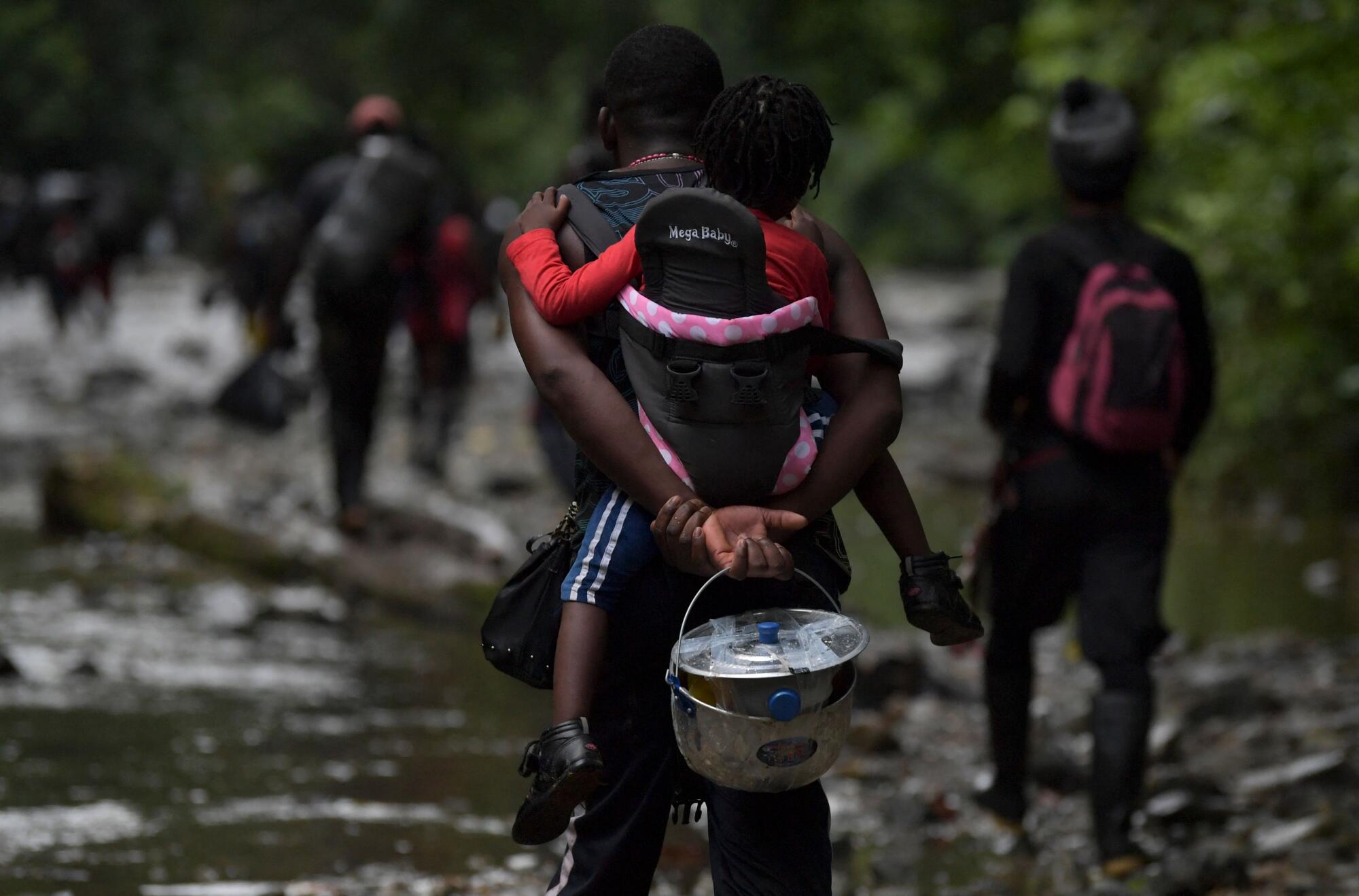 A Haitian migrant man carries a toddler as she crosses the jungle of the Darien Gap