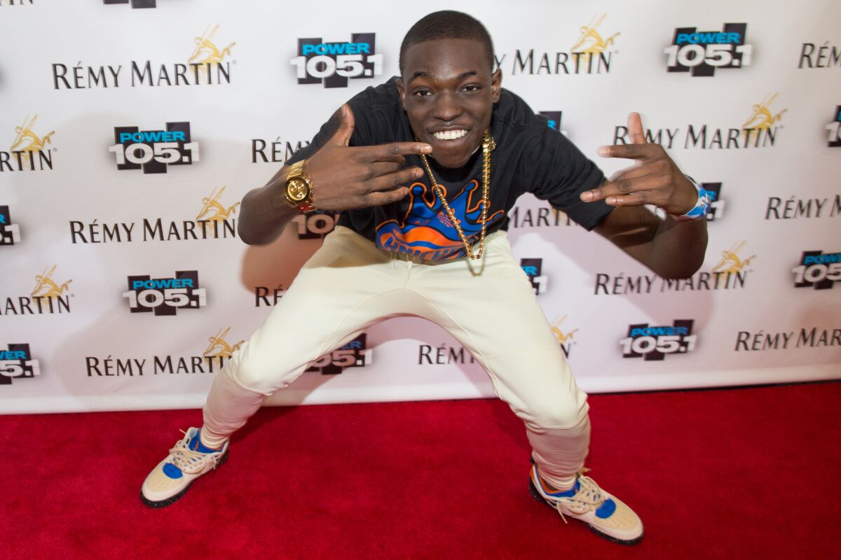 Bobby Shmurda poses on the red carpet wearing a gold chain, black shirt and white sweatpants