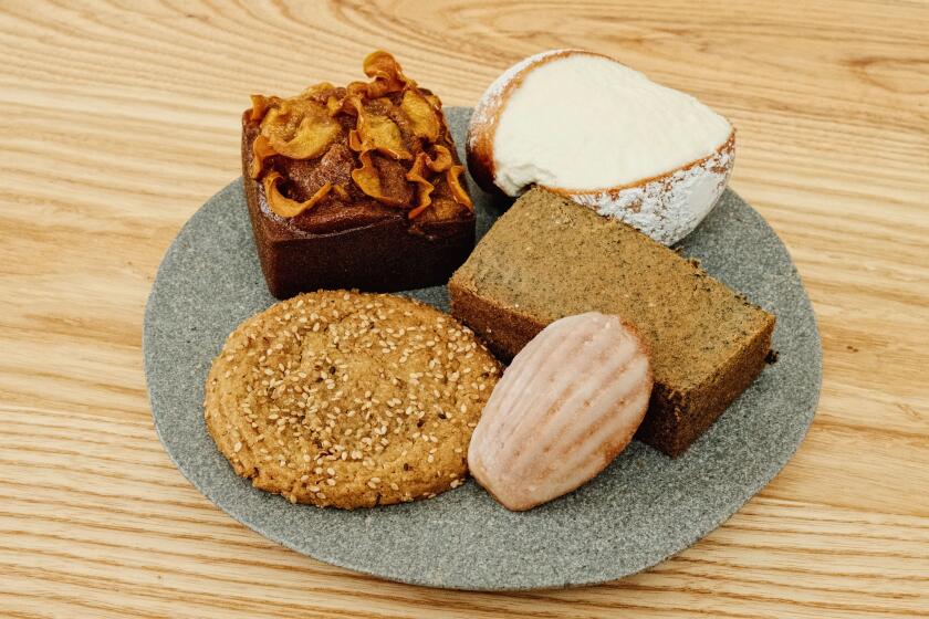 Five pastries (cream bun, mochi cake, cookies and persimmon cake) on a ceramic plate on wood table at Modu in Highland Park