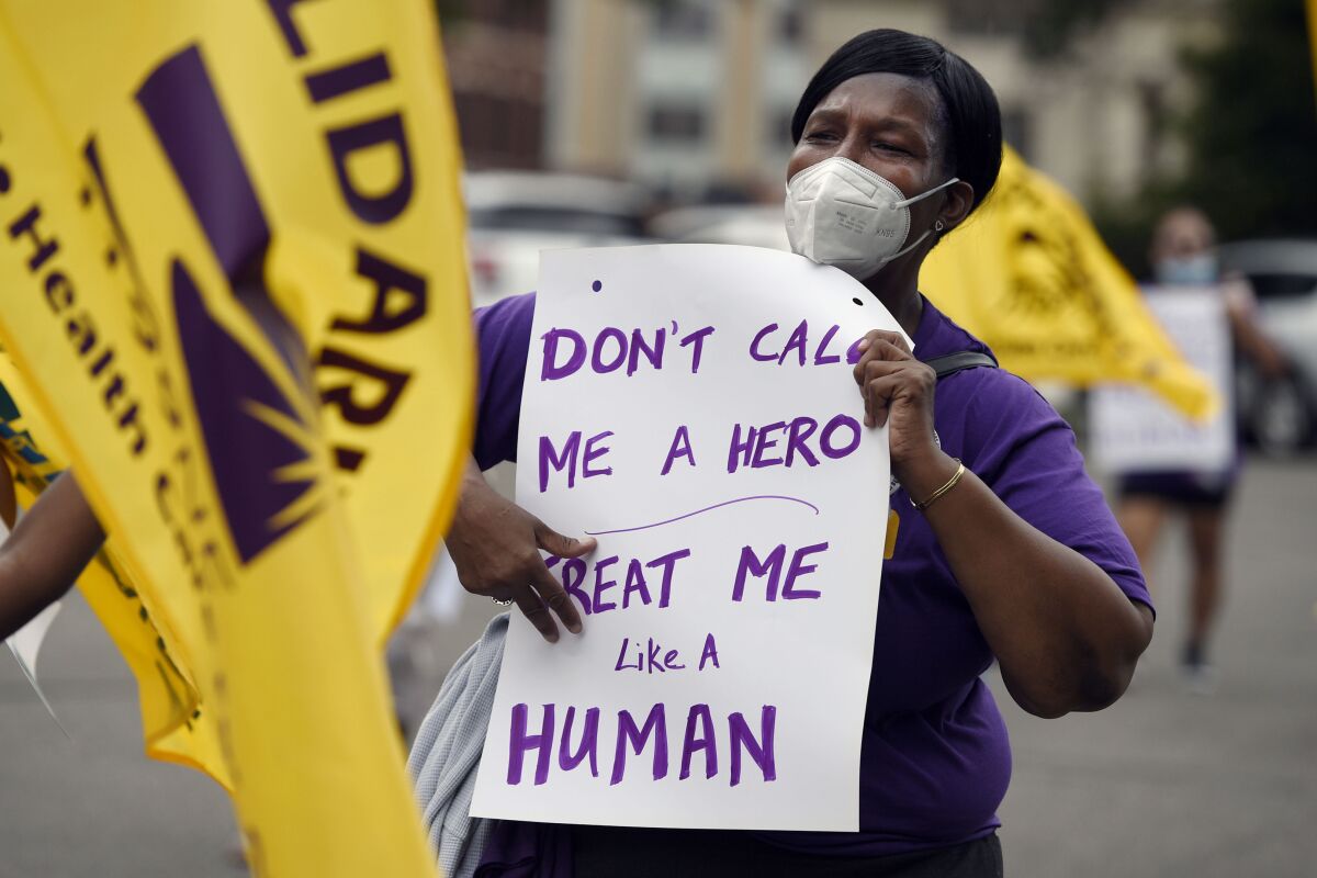 A protesting healthcare worker holds a sign reading, "Don't call me a hero - treat me like a human."
