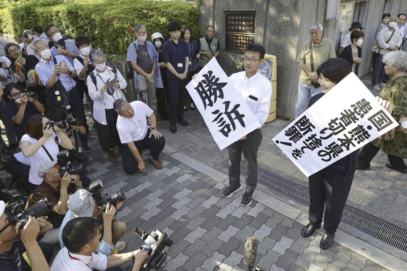The banners, one of them reading "Victory" are shown by lawyers following the verdict outside the Osaka district court in Osaka, western Japan, Wednesday, Sept. 27, 2023. The court on Wednesday ordered the central government, the Kumamoto prefecture and a chemical company to recognize more than 120 plaintiffs as patients of the decades-old Minamata mercury poisoning and pay compensation they have been denied because they developed symptoms after moving away from the region. (Kyodo News via AP)