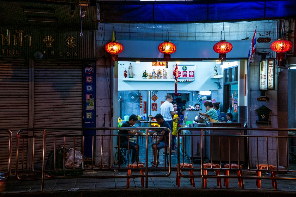 People in a small restaurant at night, viewed from the street outside.