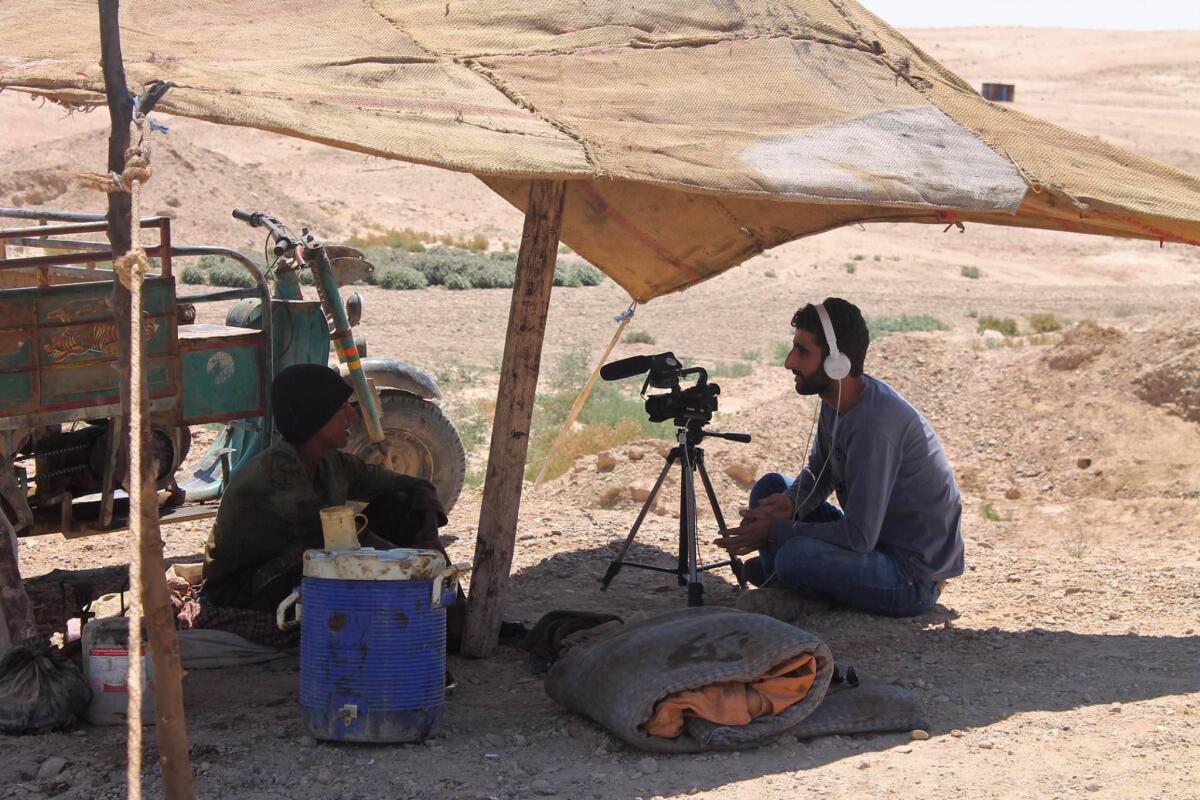 A man wearing headphones, right, interviewing another man beneath a makeshift shelter