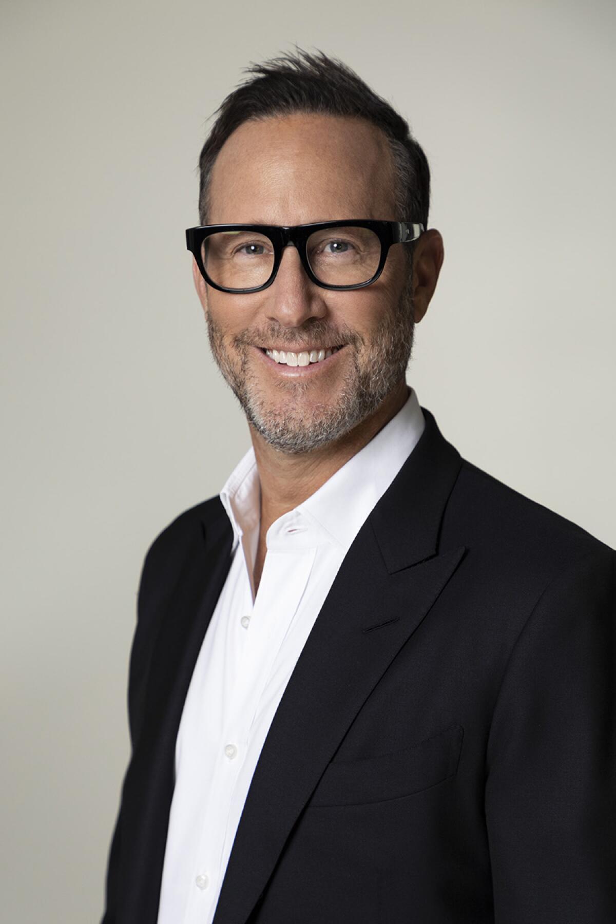 A man smiling in a suit and glasses.