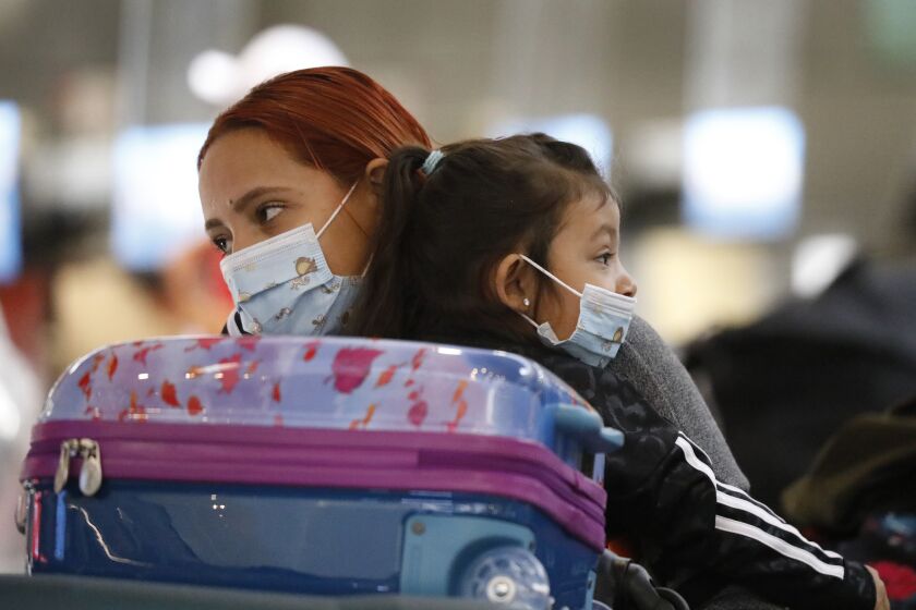 LOS ANGELES, CA - NOVEMBER 16: Passenger Karen Alvarez comforts her 3-year-old daughter Mercedez Gomez as they wait in line at the Tom Bradley International Terminal at LAX before their flight to Nicaragua on Monday November 16, 2020 as weekly coronavirus cases have doubled in just the last month around the state, and Los Angeles County had the grim distinction of recording more than 6,800 cases this weekend alone, an alarming spike that has officials talking about more restrictions. California officials are urging those who do head out of state to self-quarantine for 14 days when they return. LAX Los Angeles Airport on Monday, Nov. 16, 2020 in Los Angeles, CA. (Al Seib / Los Angeles Times