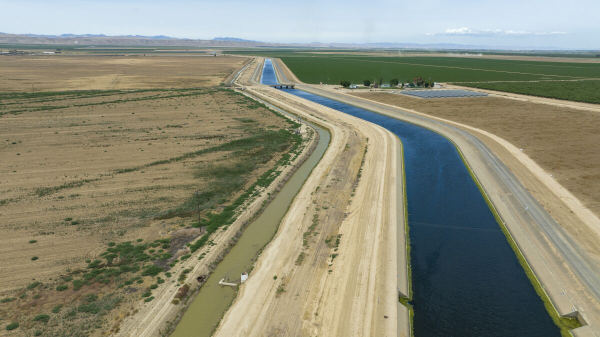 A canal of water runs through land containing crops to the right and barren land to the left.