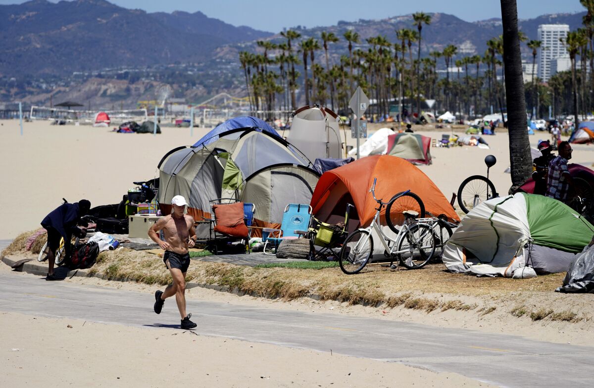FILE - A jogger runs past a homeless encampment in the Venice Beach section of Los Angeles on June 8, 2021. The city and county of Los Angeles are seeking dismissal of a sweeping lawsuit about homelessness that demands local government find shelter for thousands of people living on the streets. Attorneys for the city and county have filed dismissal motions in federal court. (AP Photo/Marcio Jose Sanchez, File)