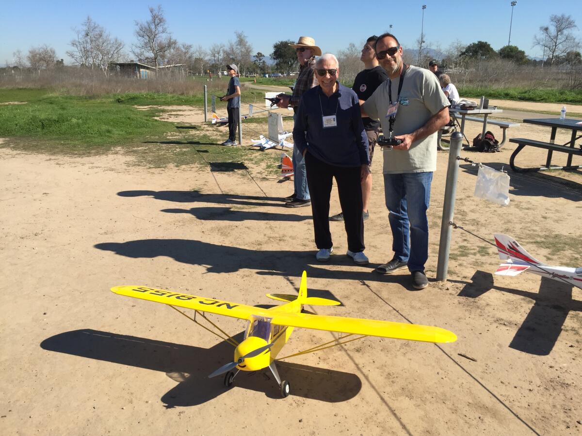 Two men pose behind a yellow model plane.