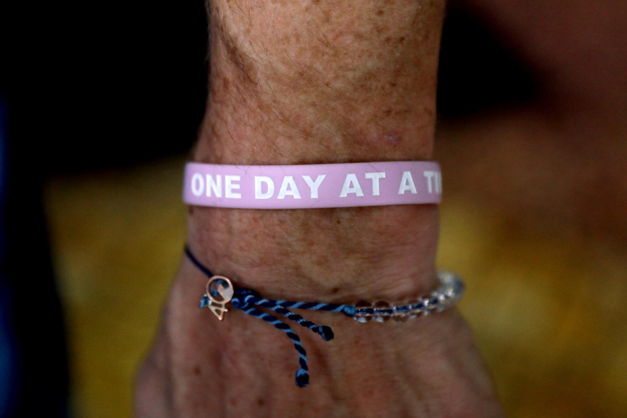 A wristband reads "One Day At A Time." 