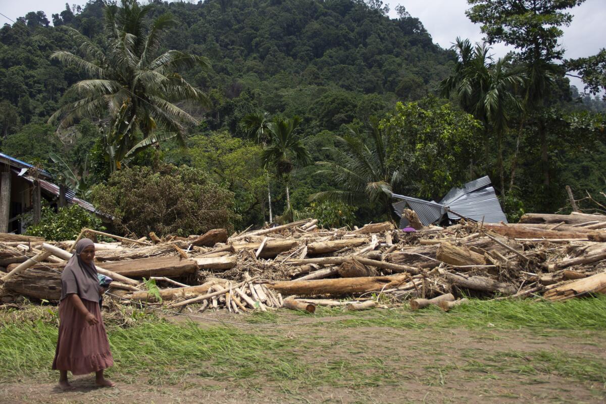 A woman walks near logs swept into a neighborhood by a flash flood in West Sumatra, Indonesia.