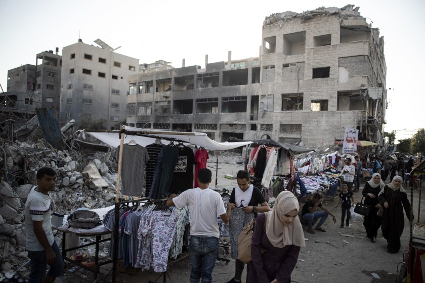 Palestinian street vendors display clothes for sale next to the rubble of destroyed buildings 