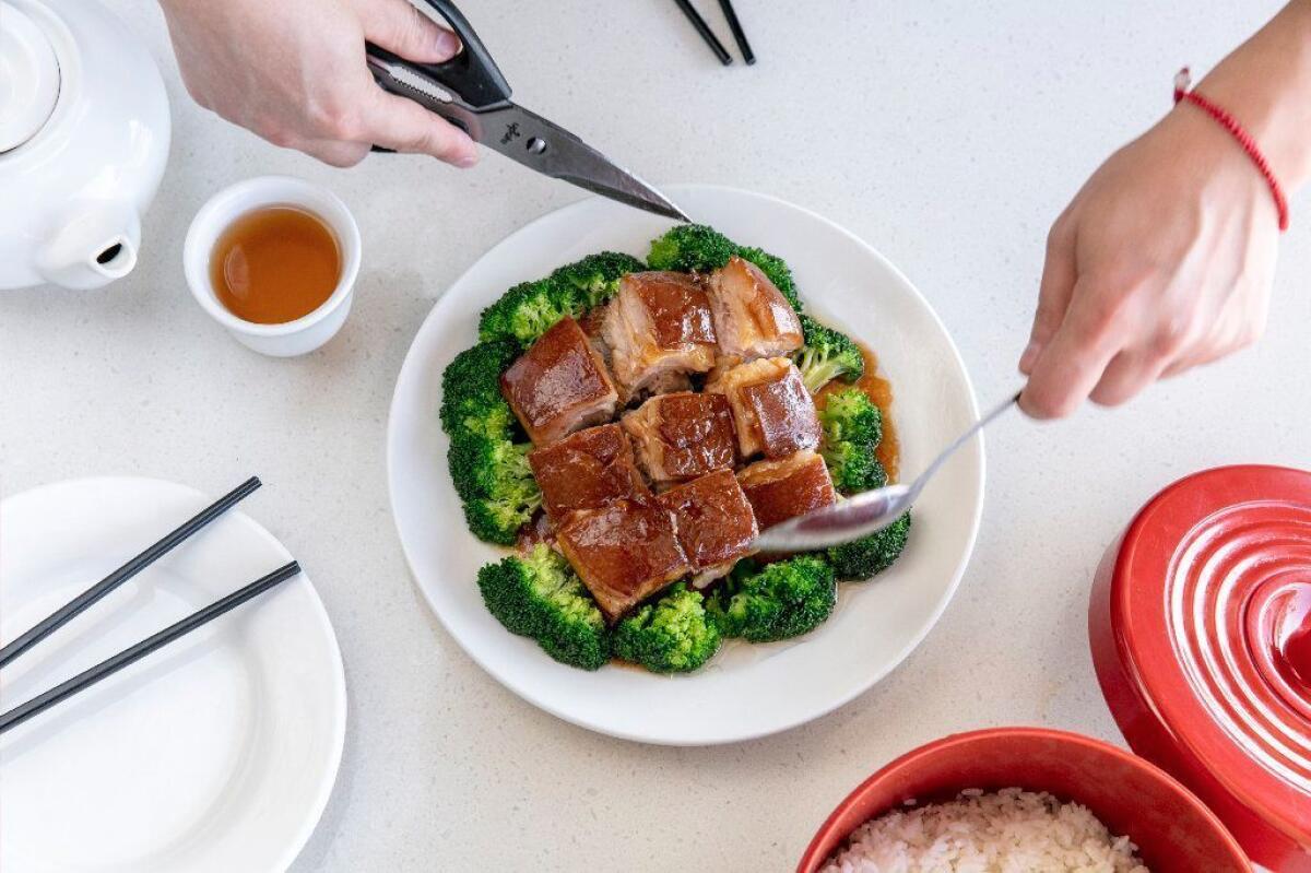 A server uses scissors to cut braised pork belly into manageable pieces.