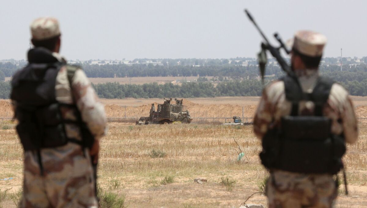 Palestinian militants of the Izzidin al-Qassam Brigade watch an Israeli bulldozer working along a fence that separates the southern Gaza Strip and Israel on June 3. Rocket fire into Israel later in the day was followed by Israeli airstrikes June 4 on Gaza.